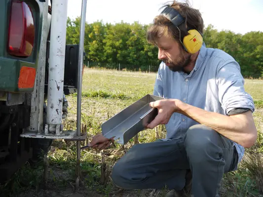 ein Mann hält ein Probenentnahmegerät in der Hand und hockt auf einem Feld