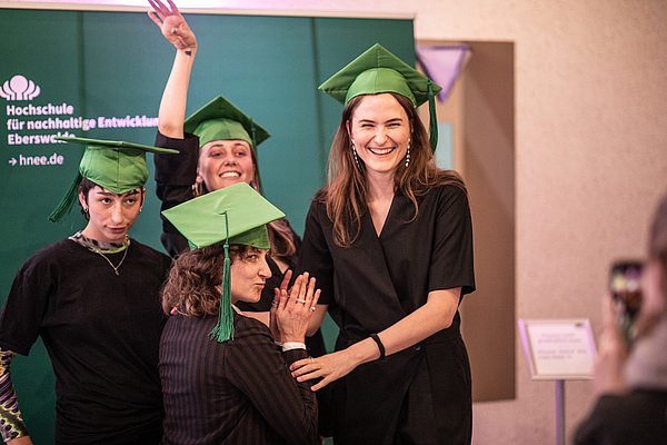 Vier junge Menschen mit grünen Doktorhüten feiern ihren Studienabschluss.