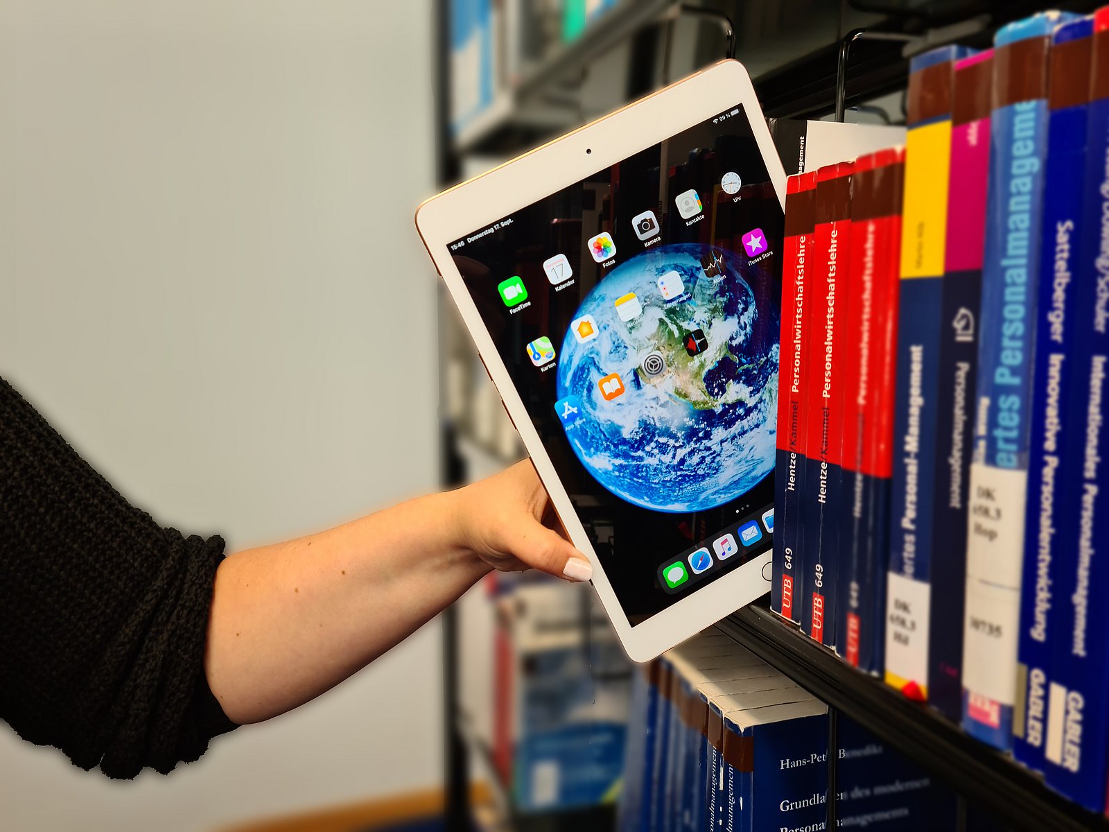 Ein Tablet wird ähnlich einem Buch in ein Bücherregal einer Fachbibliothek gestellt.