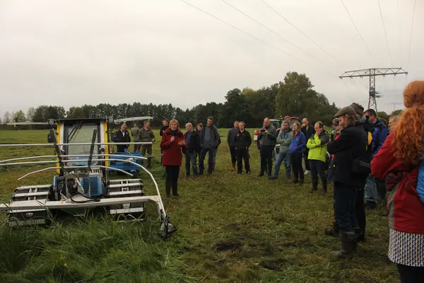 mehre Menschen stehen im Halbkreis um eine Landmaschine und hören der Erklärung zu