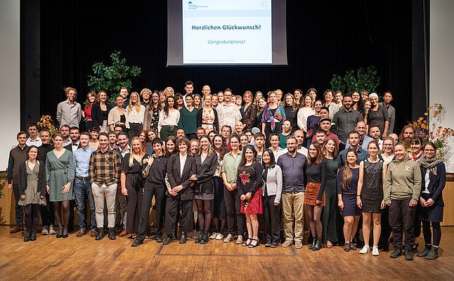 Auf der Bühne im Haus Schwärzetal stehen die Alumni der Hochschule für nachhaltige Entwicklung Eberswalde aus dem Jahr 2023