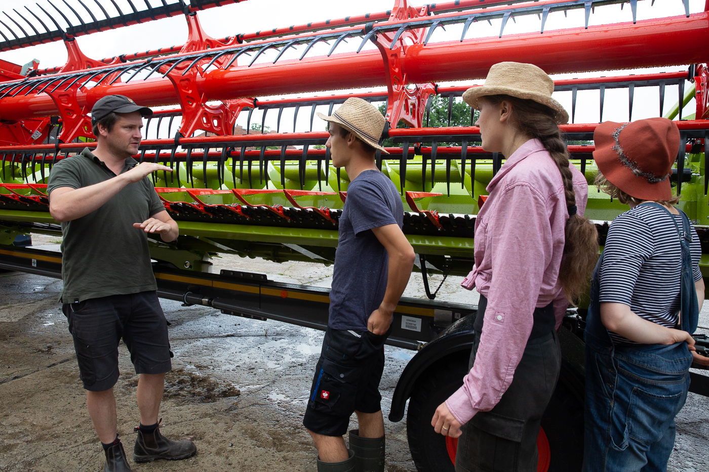Ein Landwirt steht vor einer landwirtschaftlichen Maschine und erläutert drei Studierenden die Einstellungen der Maschine.